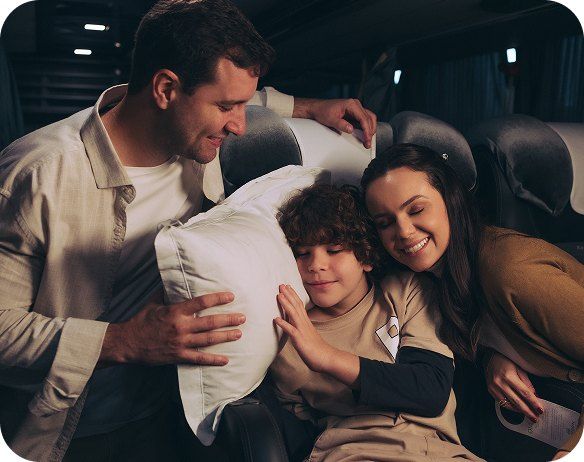 Família sorrindo e descansando com travesseiro dentro do ônibus Cabine Cama
